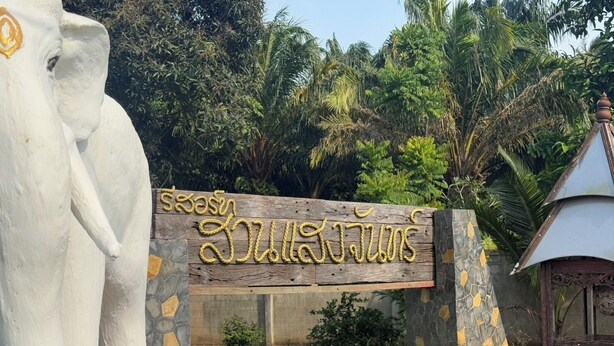 A sign with text in a non-Latin script, a white elephant statue, and a building with a stone facade. - Suan Sang Chan Riverside Resort (Chumphon)