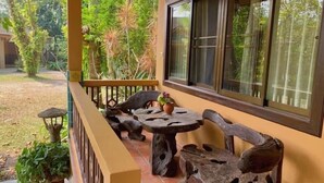 Un área de estar al aire libre con techo, mobiliario de madera rústica y vistas a un exuberante jardín.
