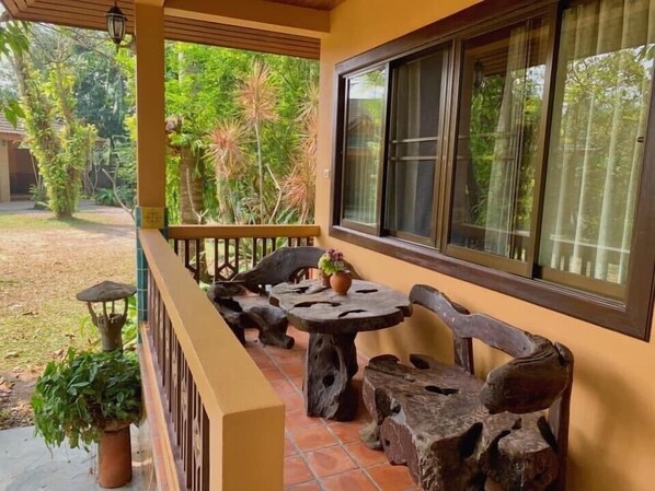A covered outdoor seating area with rustic wooden furniture and a view of a lush garden. - Suan Sang Chan Riverside Resort (Chumphon)