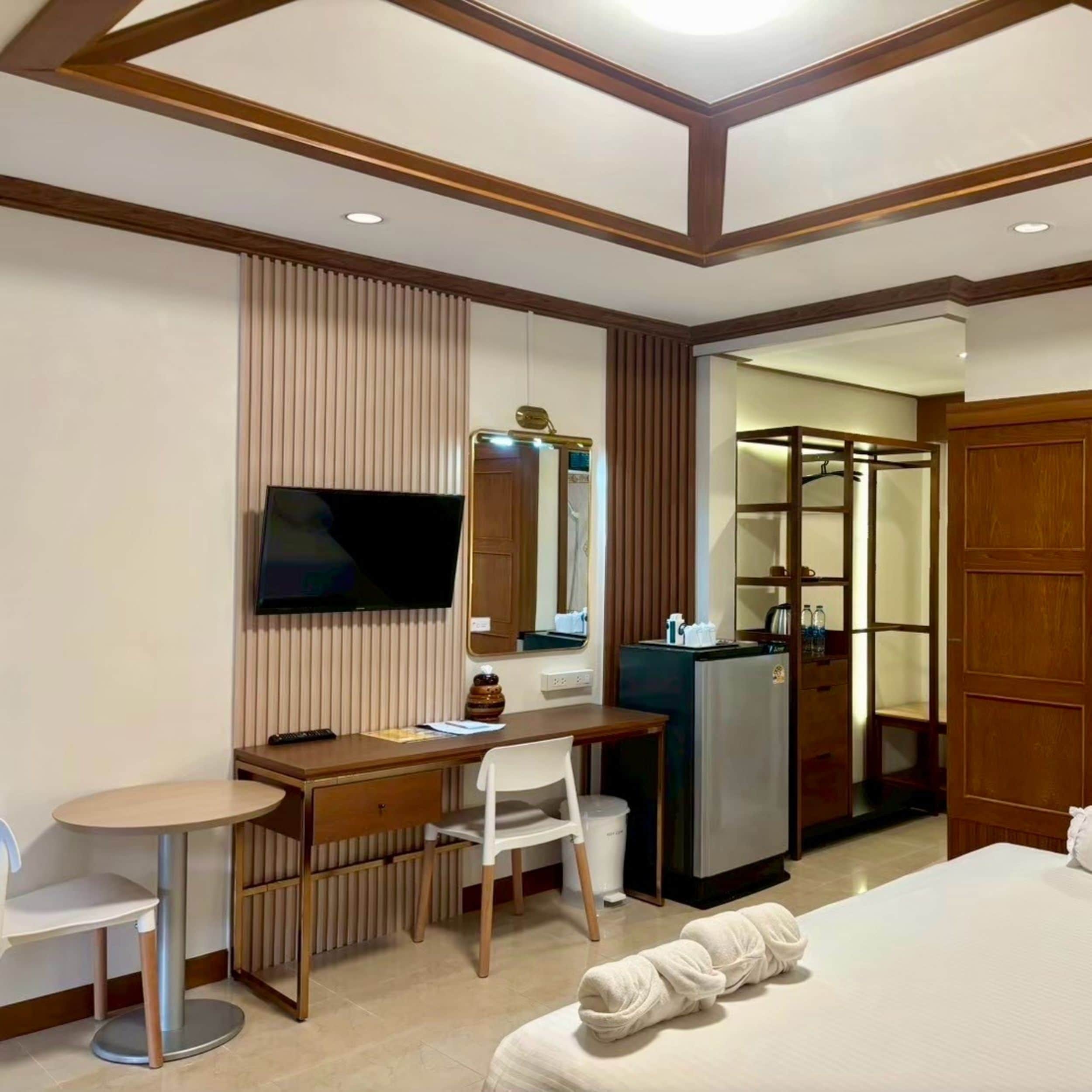 A hotel room with a bed, a desk with a chair, a television, a mirror, and a wardrobe.