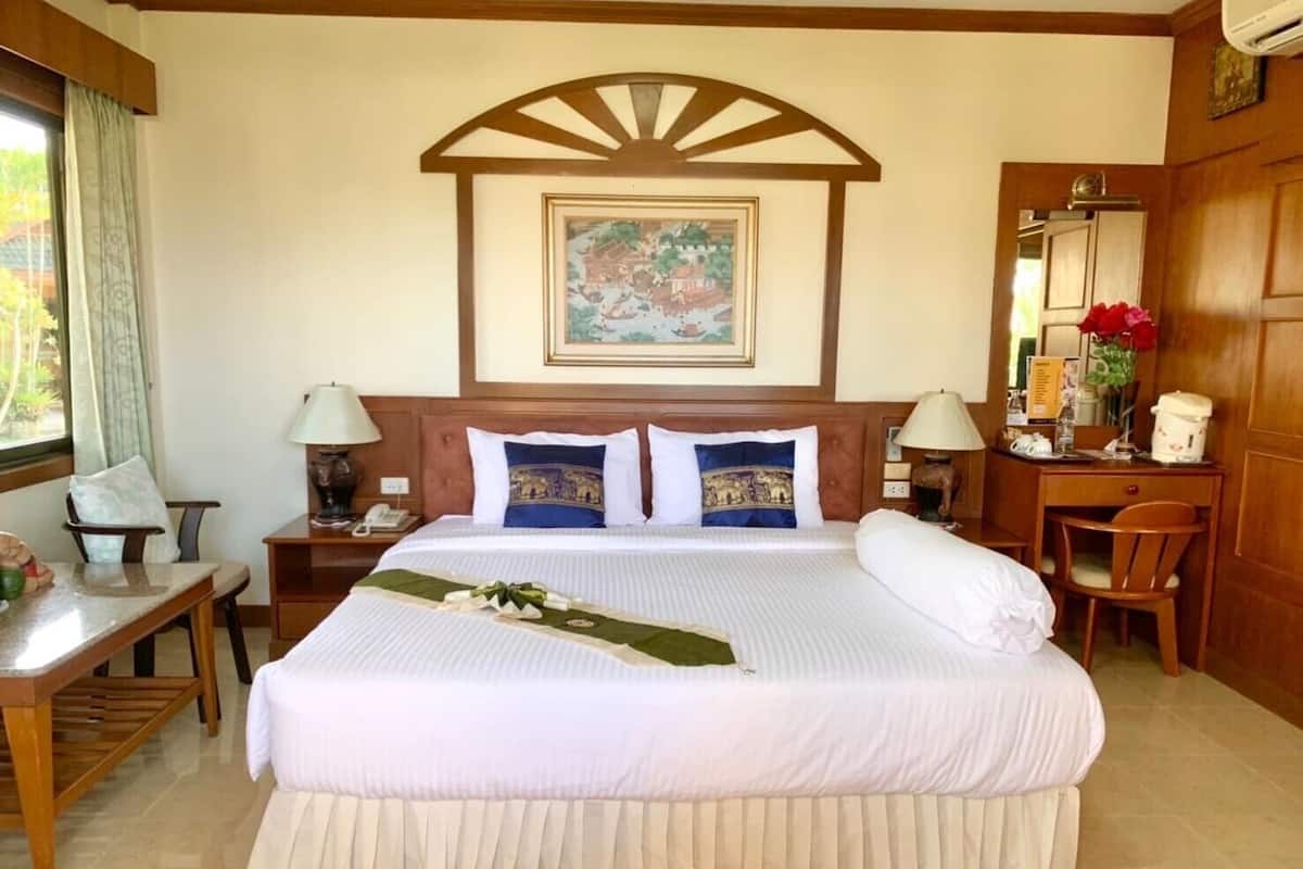 A hotel room with a large bed, two bedside tables, a desk, a chair, a mirror, and a window with curtains.