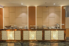 Zona de recepción de hotel con mostrador de mármol, cámara de seguridad y espacio para desayuno tipo buffet.