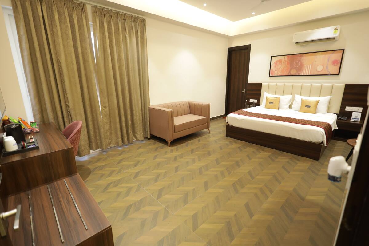 A hotel room with a bed, a sofa, a desk, and a large window with curtains.