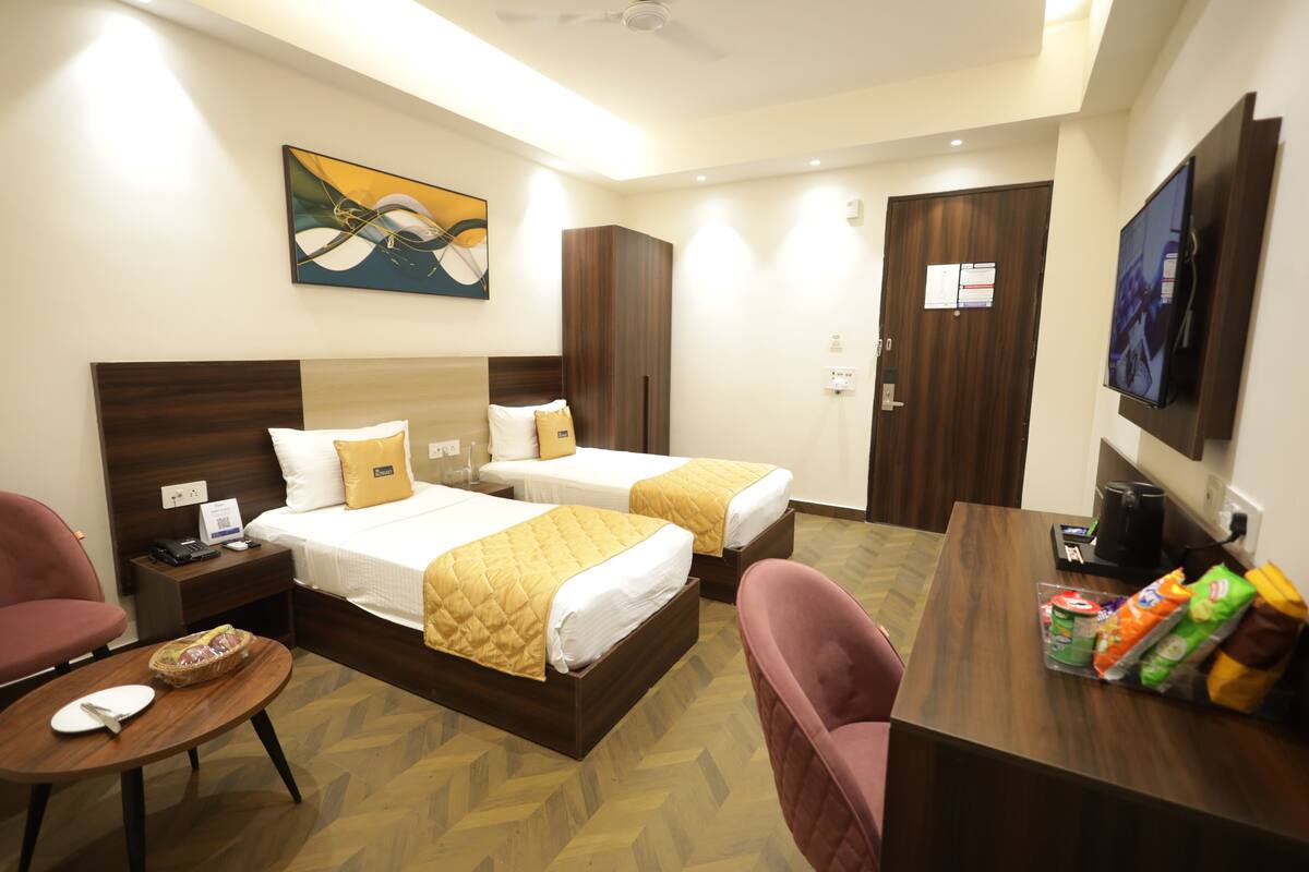 A hotel room with two beds, a desk, a television, and a painting on the wall.