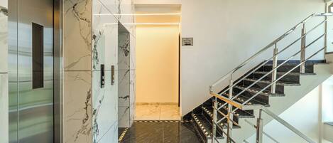 Interior moderno de hotel con un ascensor de mármol, una escalera con barandillas metálicas y un cartel que indica las habitaciones 416-417.