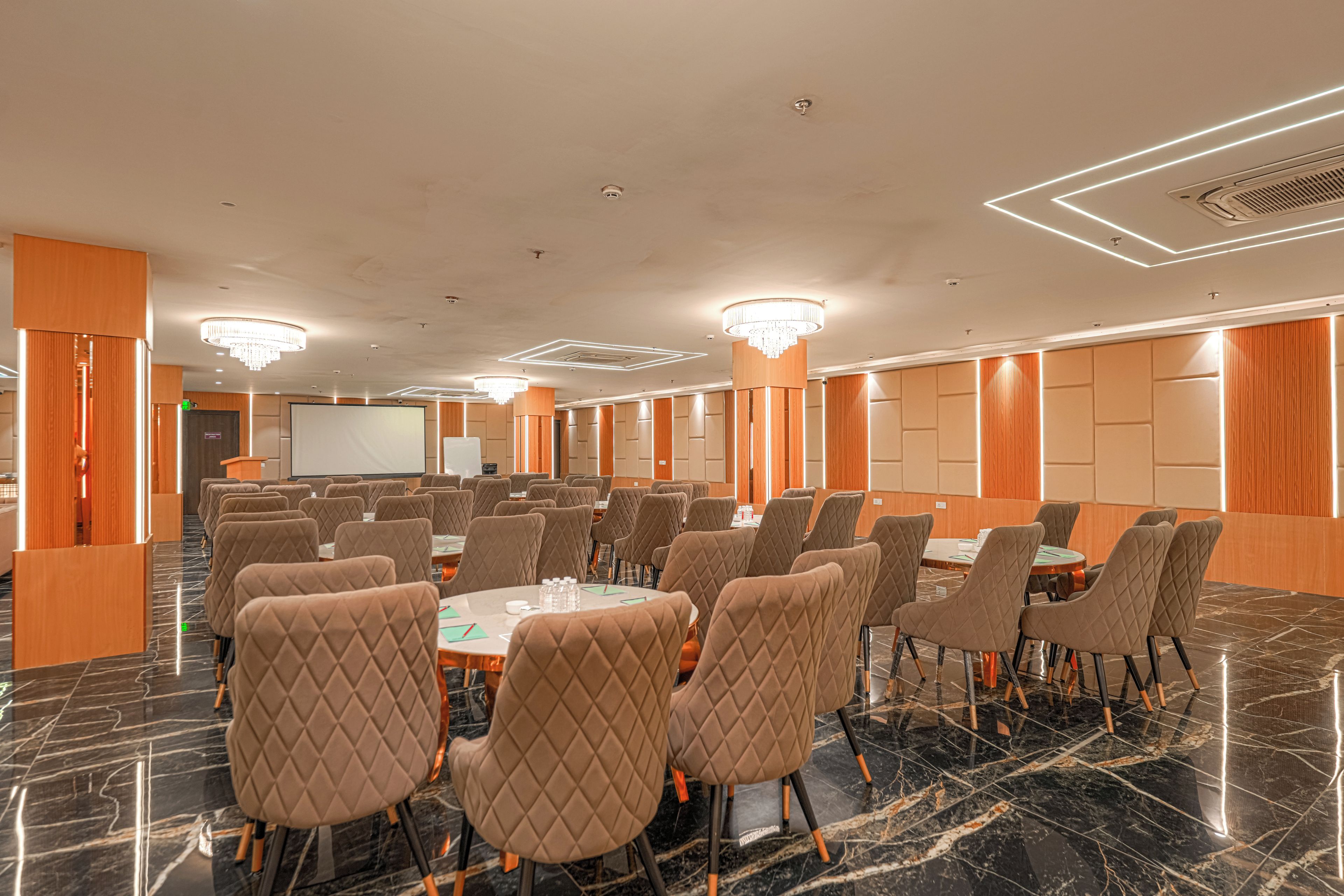 A conference room with a large screen, multiple tables, and chairs.
