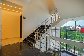 A modern interior with a staircase leading to a balcony overlooking a cityscape. - The Altruist Gurugram Hotel (Gurugram)