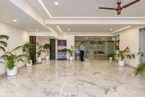 A modern lobby with marble flooring, potted plants, a ceiling fan, and a banner for 'TENNAT ALTRUIST'. - The Altruist Gurugram Hotel (Gurugram)