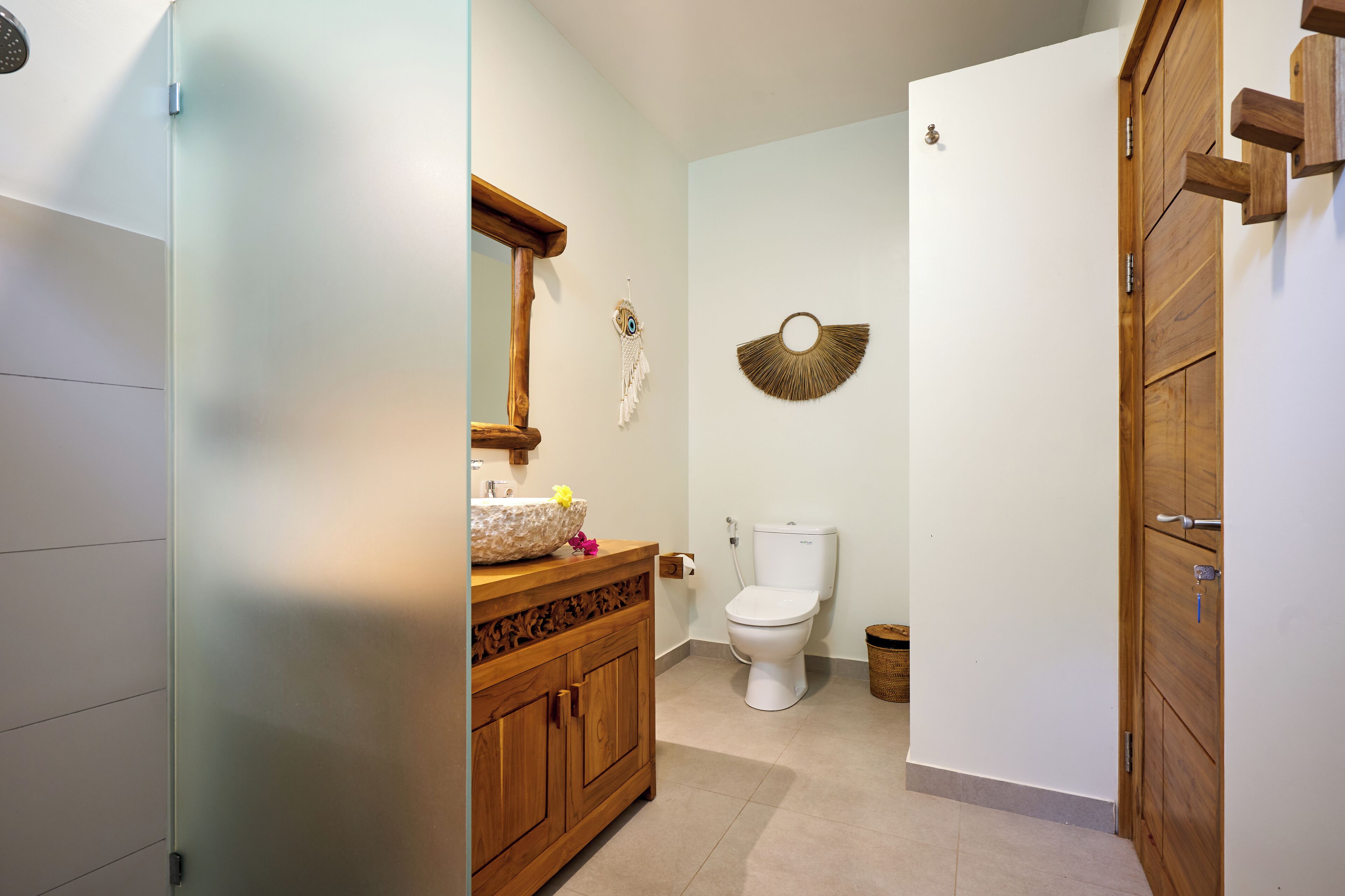 A bathroom with a wooden vanity, a round mirror, a white toilet, and a wall-mounted decorative item.