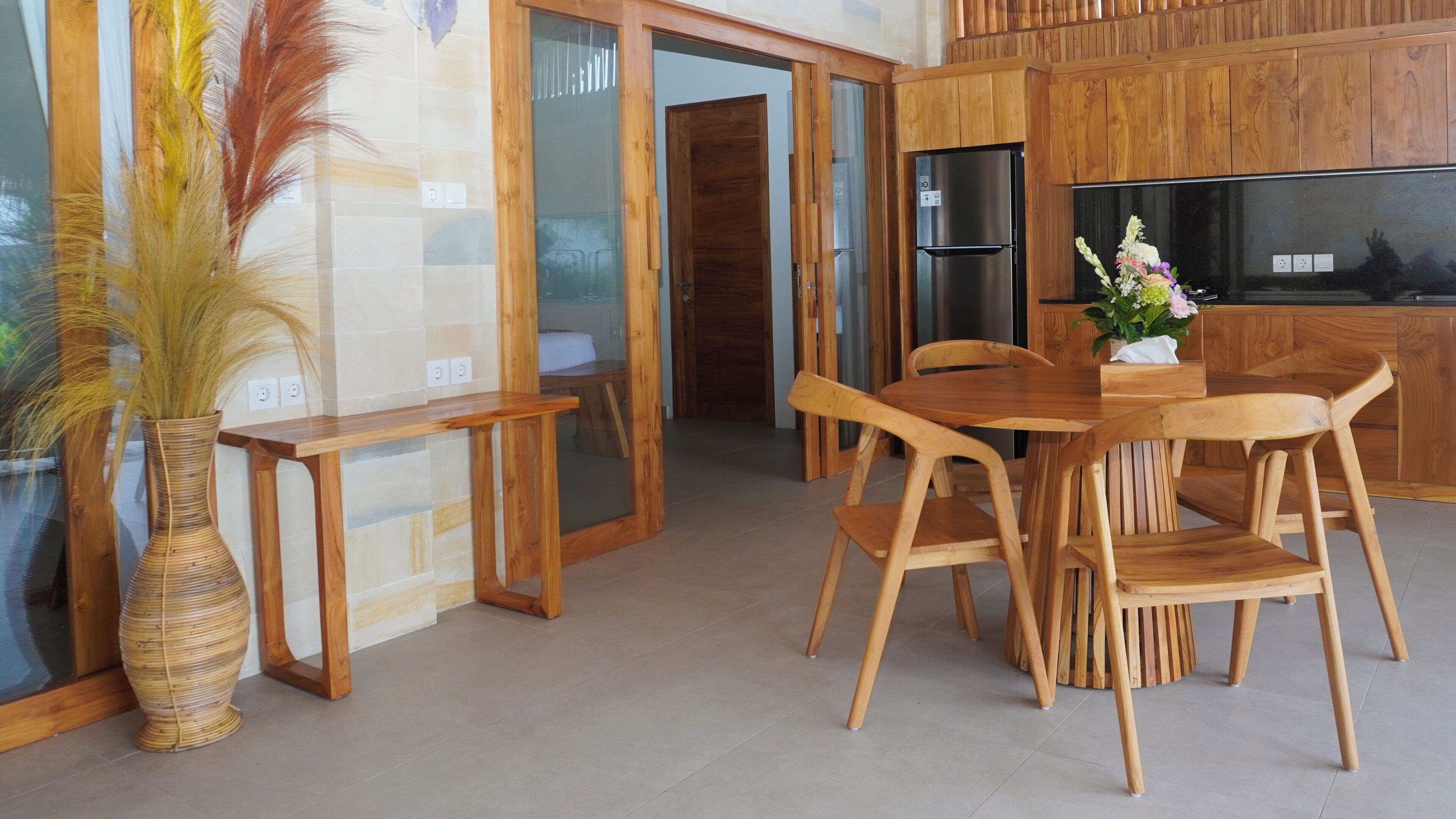 A modern kitchen with wooden cabinets, a dining table with chairs, and a vase with dried plants.
