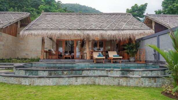 Un complejo turístico con villas de techo de paja, una piscina y un jardín exuberante.
