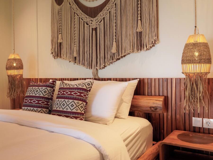 Un lit avec des coussins à motifs, une décoration murale en macramé et deux lampes suspendues.