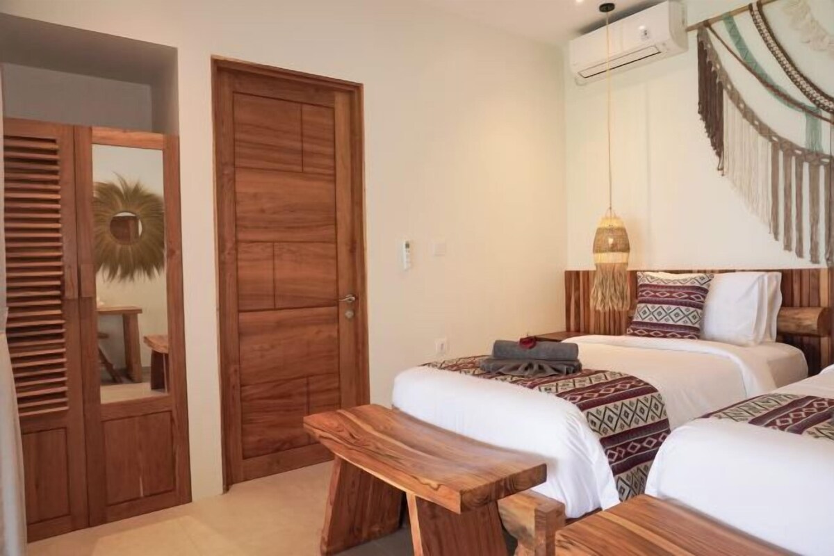 A bedroom with two beds, a wooden bench, a wardrobe, and a wall-mounted air conditioner.