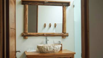 Un baño con espejo de marco de madera, lavabo de piedra y tocador de madera.