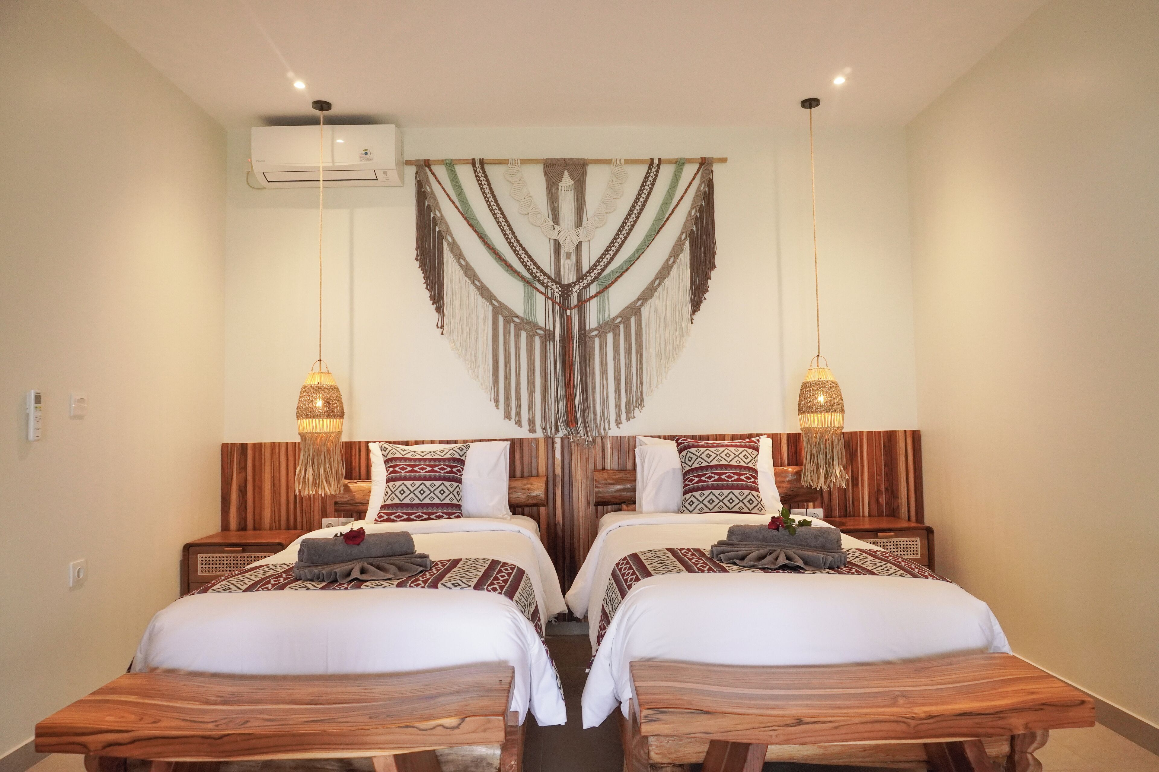 A room with two wooden beds, a hanging macrame decoration, and two pendant lights.