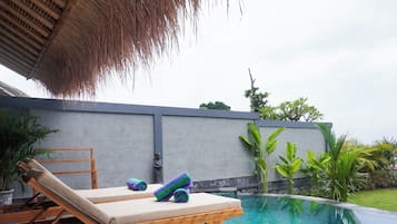 Relax by the tranquil pool surrounded by lush tropical plants and a shaded thatched roof.