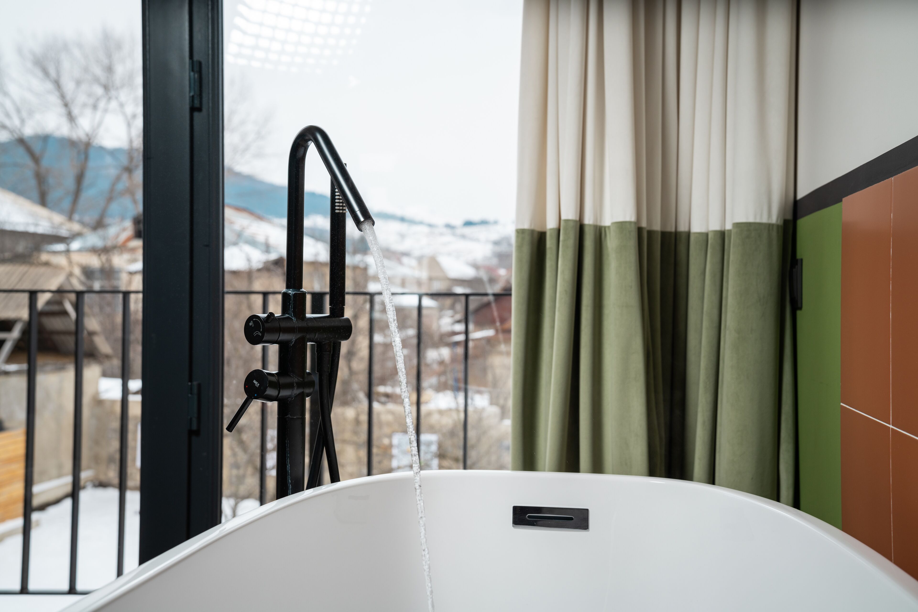 A bathroom with a bathtub, a window with curtains, and a view of a snowy landscape.