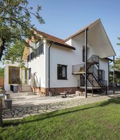 Una casa de dos pisos con balcón, escalera y mobiliario exterior.