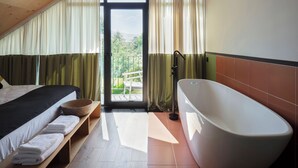 A bedroom with a bed, a bench with towels, a bathtub, and a balcony with curtains. - Major's House Hotel (Step'anavan)