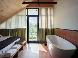 Un dormitorio con cama, un banco con toallas, una bañera y un balcón con cortinas.
