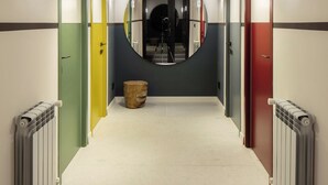 A hallway with a central circular mirror, flanked by doors in various colors, and radiators on either side. - Major's House Hotel (Step'anavan)