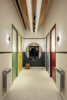 Un pasillo con un espejo circular central, flanqueado por puertas de varios colores, y radiadores a ambos lados.