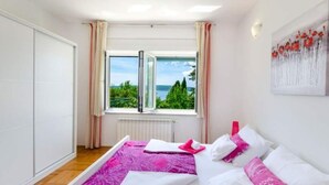 Een slaapkamer met een groot raam, een bed met witte en roze beddengoed, en uitzicht op groen en water.