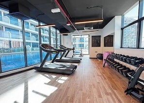 A gym with treadmills, dumbbells, and large windows overlooking a body of water. - Bloomfield Luxury Studio Samana Golf (Dubai)