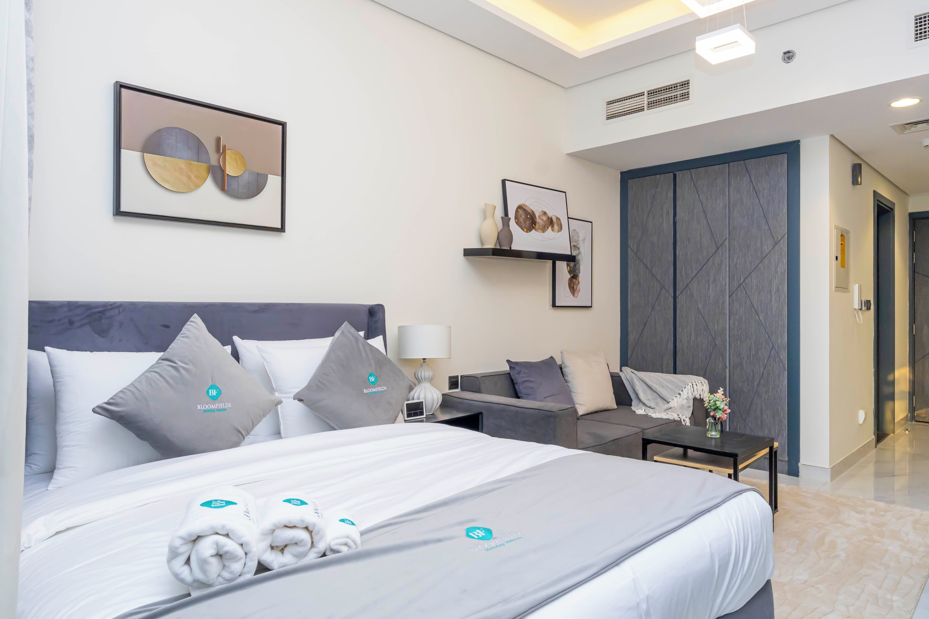 Une chambre d’hôtel moderne, dotée d’un grand lit, d’un canapé, d’une petite table et d’une étagère murale agrémentée d’objets décoratifs.