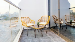 A balcony with wicker chairs and a small table, large windows offering a city view.