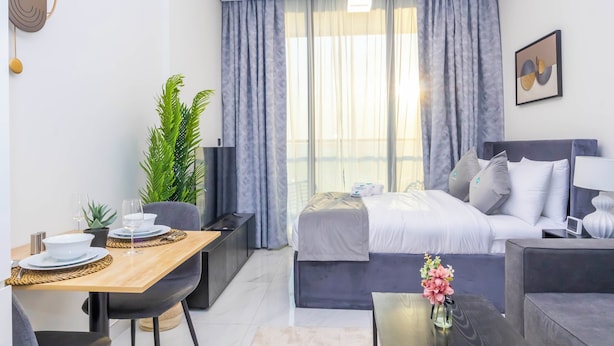 A modern hotel room with a bed, bedside table, and a dining area with a table set for two.