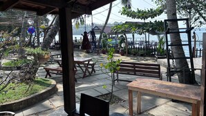An outdoor patio with wooden tables and benches, surrounded by potted plants and trees.