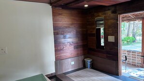 A room with wooden walls, a tiled floor, a small trash bin, and a door leading outside.