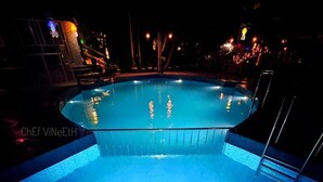 A swimming pool at night with clear water, surrounded by a poolside area with steps and railings.