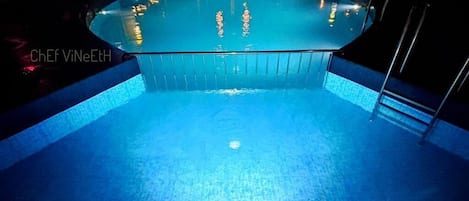 A swimming pool at night with clear water, surrounded by a poolside area with steps and railings.