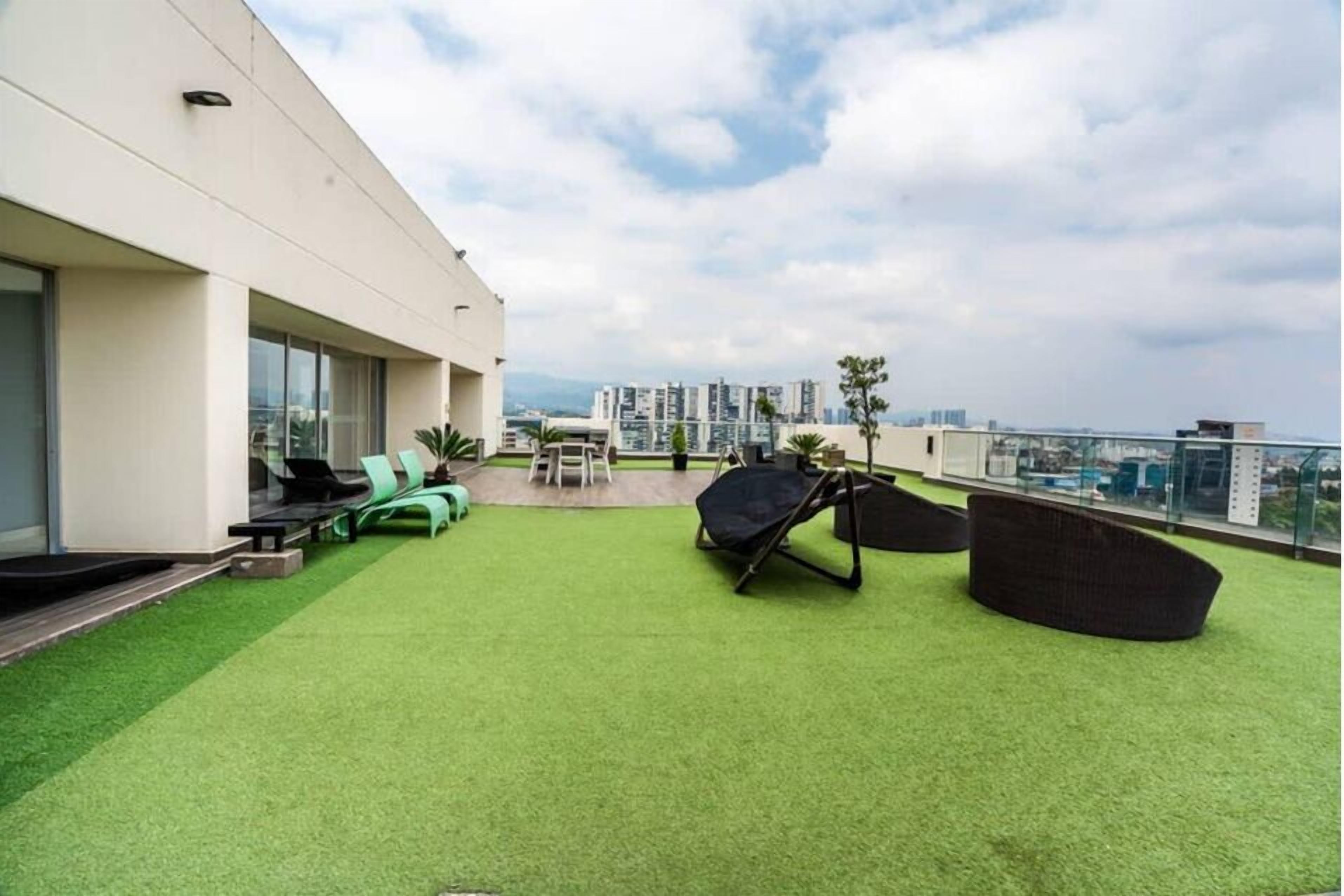 A rooftop terrace with artificial grass, outdoor furniture, and a view of the cityscape.