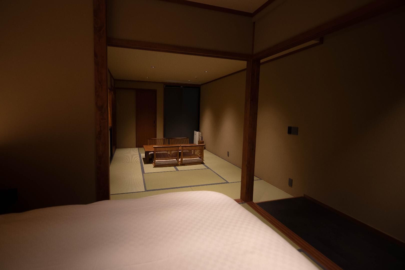 A traditional Japanese room with tatami flooring, a low wooden bed, and a futon in the background.