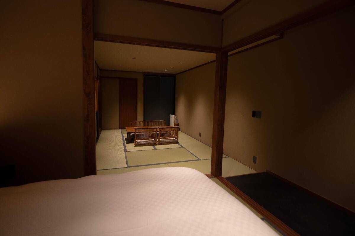 A traditional Japanese room with tatami flooring, a low wooden bed, and a futon in the background.