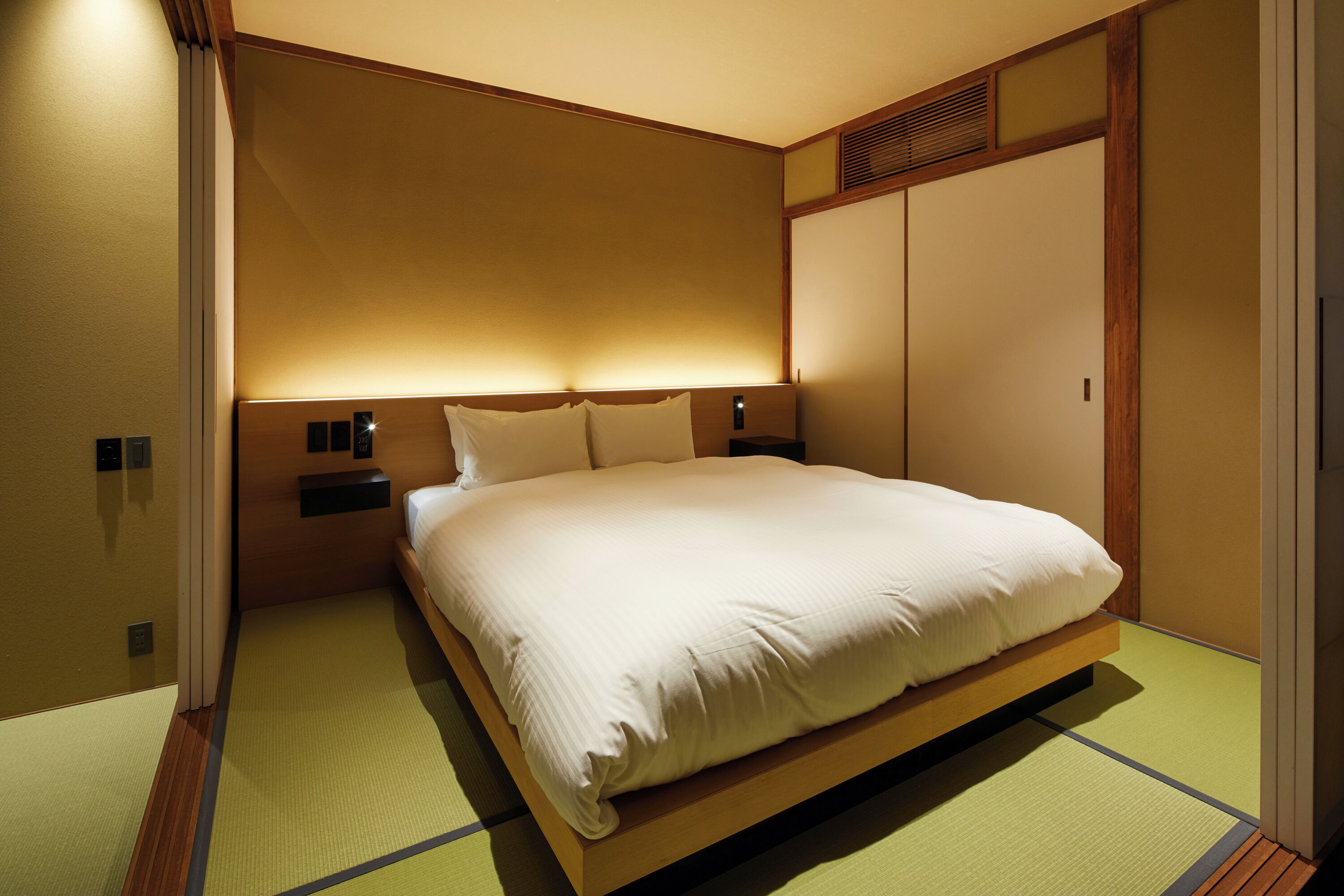 A hotel room with a bed, bedside tables, and a traditional sliding door.
