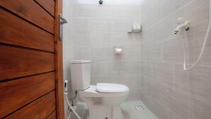 A small, modern bathroom with a wooden door, a white toilet, a showerhead, and a toilet paper holder. - DMY Guest House Nusa Penida (Penida Island)