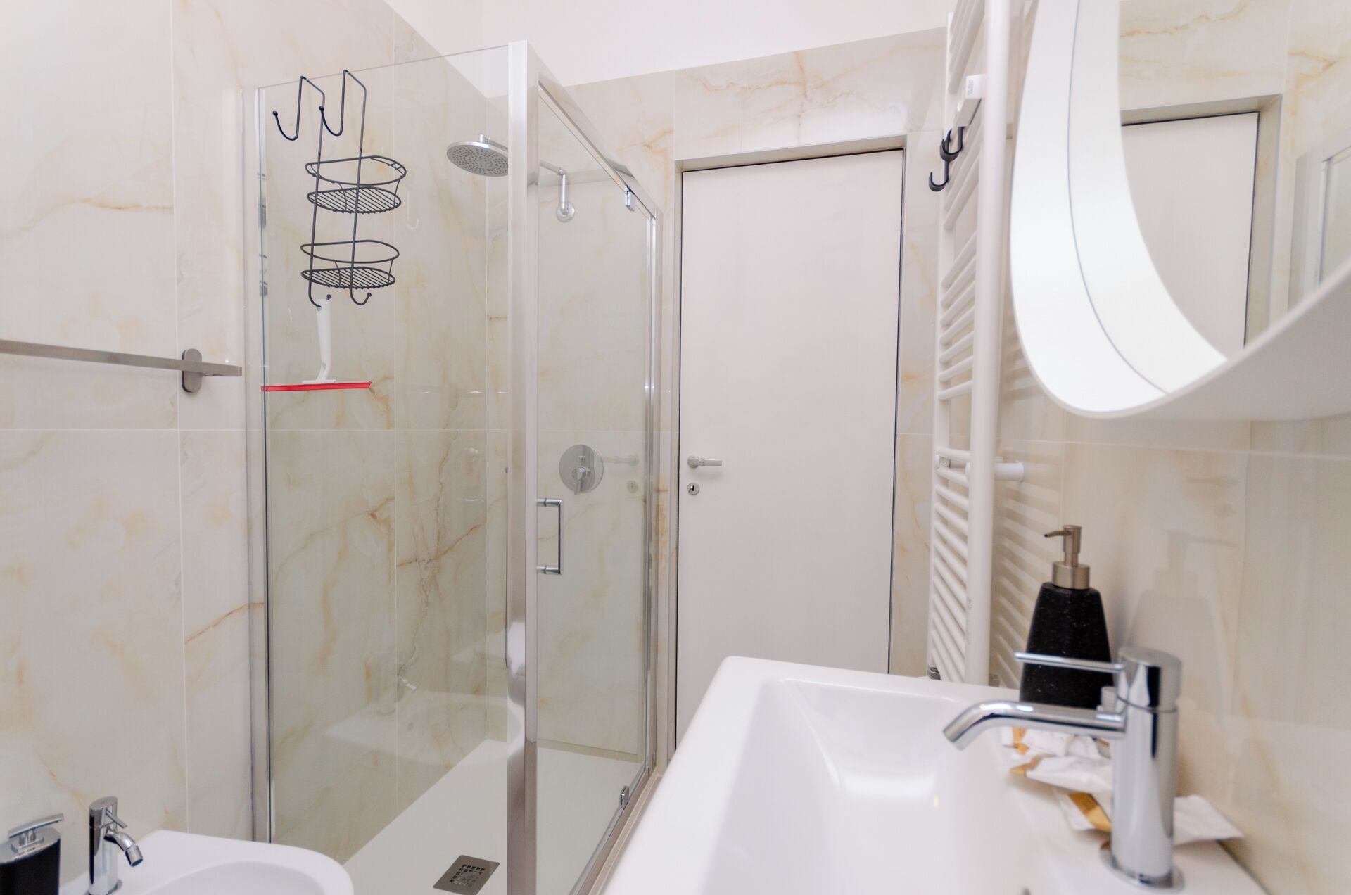 Un baño moderno con cabina de ducha de vidrio, lavamanos blanco con grifo plateado y un espejo grande.