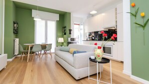 Una sala de estar moderna con sofá, mesa de comedor y sillas. Cuenta con una zona de cocina con armarios y estufa.