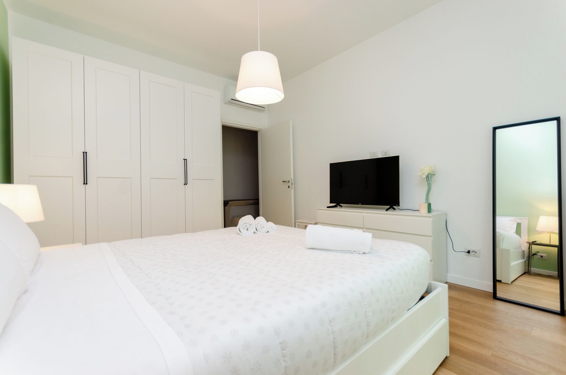 A bedroom with a bed, a television, a mirror, and a wardrobe.