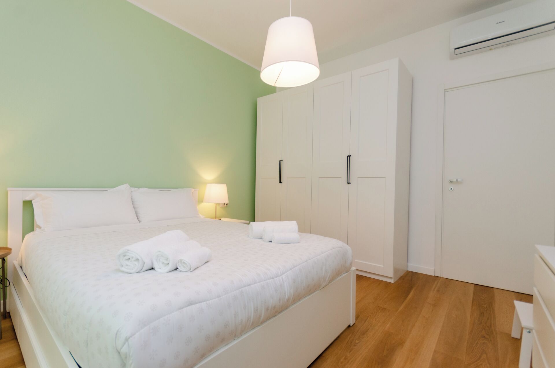 Un lit bien fait, avec des serviettes pliées, une lampe de chevet et une armoire à plusieurs portes.