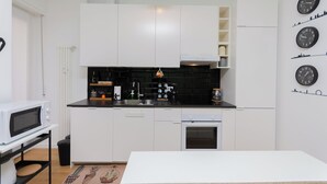 Una cocina moderna con armarios blancos, encimera negra y horno integrado. Hay relojes de pared y un microondas en la encimera.
