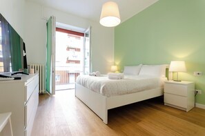 A bedroom with a bed, bedside tables, a dresser, and a window with a view of buildings. - VivimiHome - Fiordalisi Home (Milan)