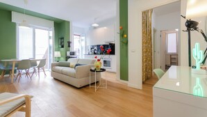 Una sala de estar moderna con sofá, mesa de comedor y sillas. Se ve una cocina al fondo con microondas y otros electrodomésticos.