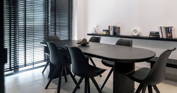 Un espace repas moderne avec une table ronde et six chaises, une bibliothèque remplie de livres et un bol décoratif posé sur la table.