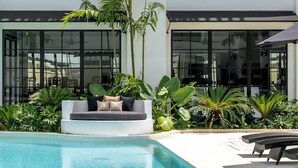Un área de piscina moderna al aire libre con una zona de estar integrada y exuberante vegetación tropical.