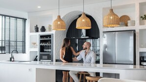 Una cocina moderna con una isla central, luces colgantes y un refrigerador de acero inoxidable.